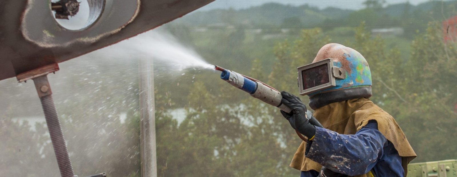 worker, sandblasting the corroded hull of a sailing vessel with a high pressure sandblasting syst